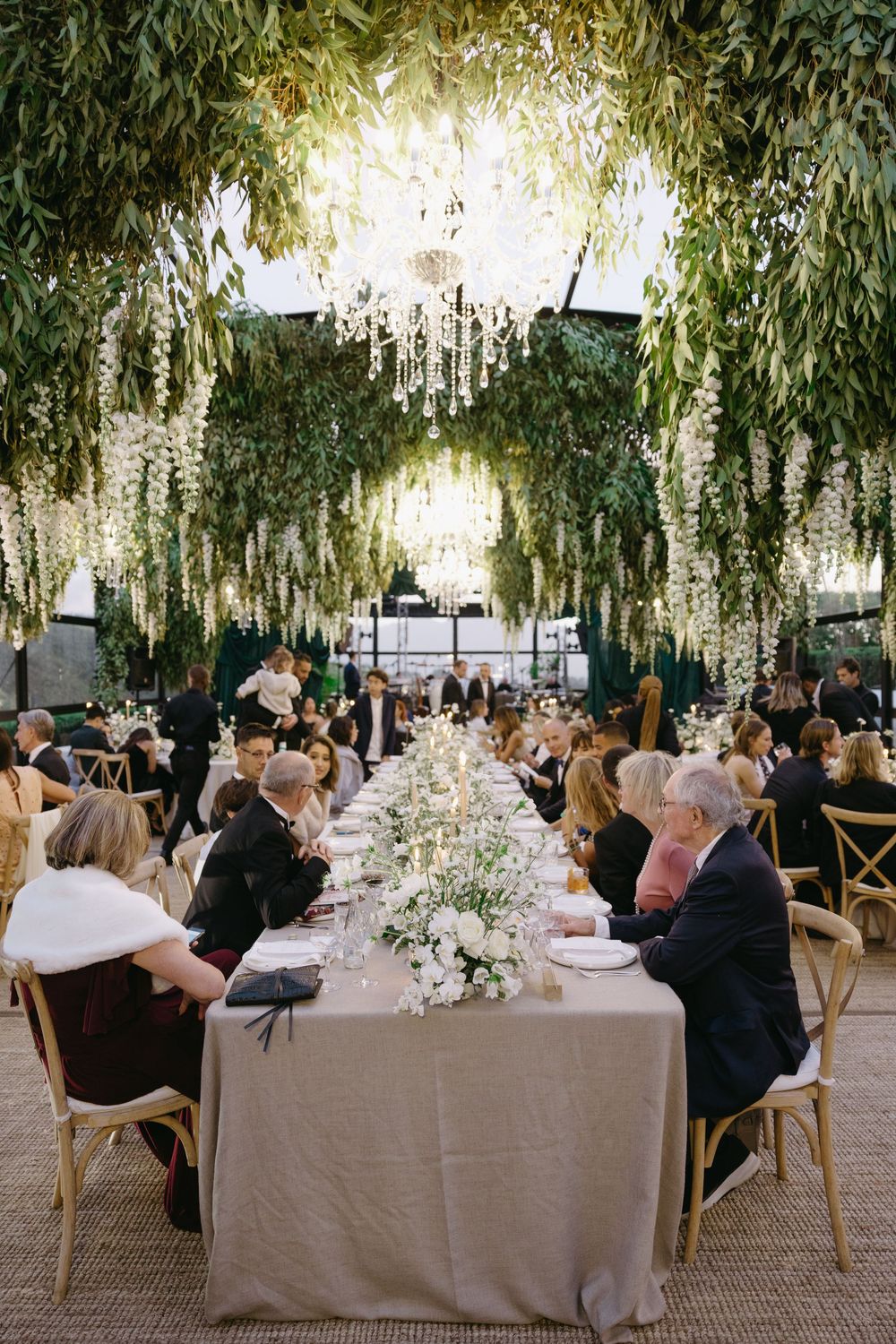 Elegant outdoor wedding reception under willow trees with long tables and white floral centerpieces.