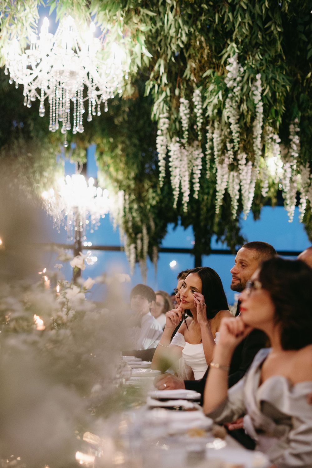 Wedding guests watch in awe under hanging floral decorations and chandeliers during an evening reception.