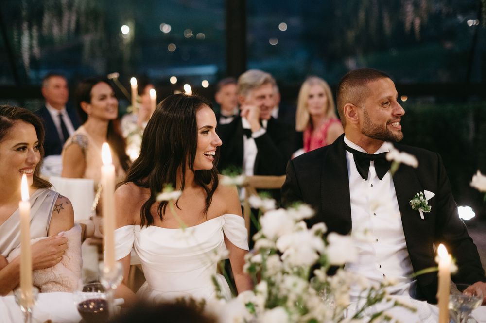 Wedding reception guests dance and celebrate on a dimly lit dance floor surrounded by elegant white floral arrangements.