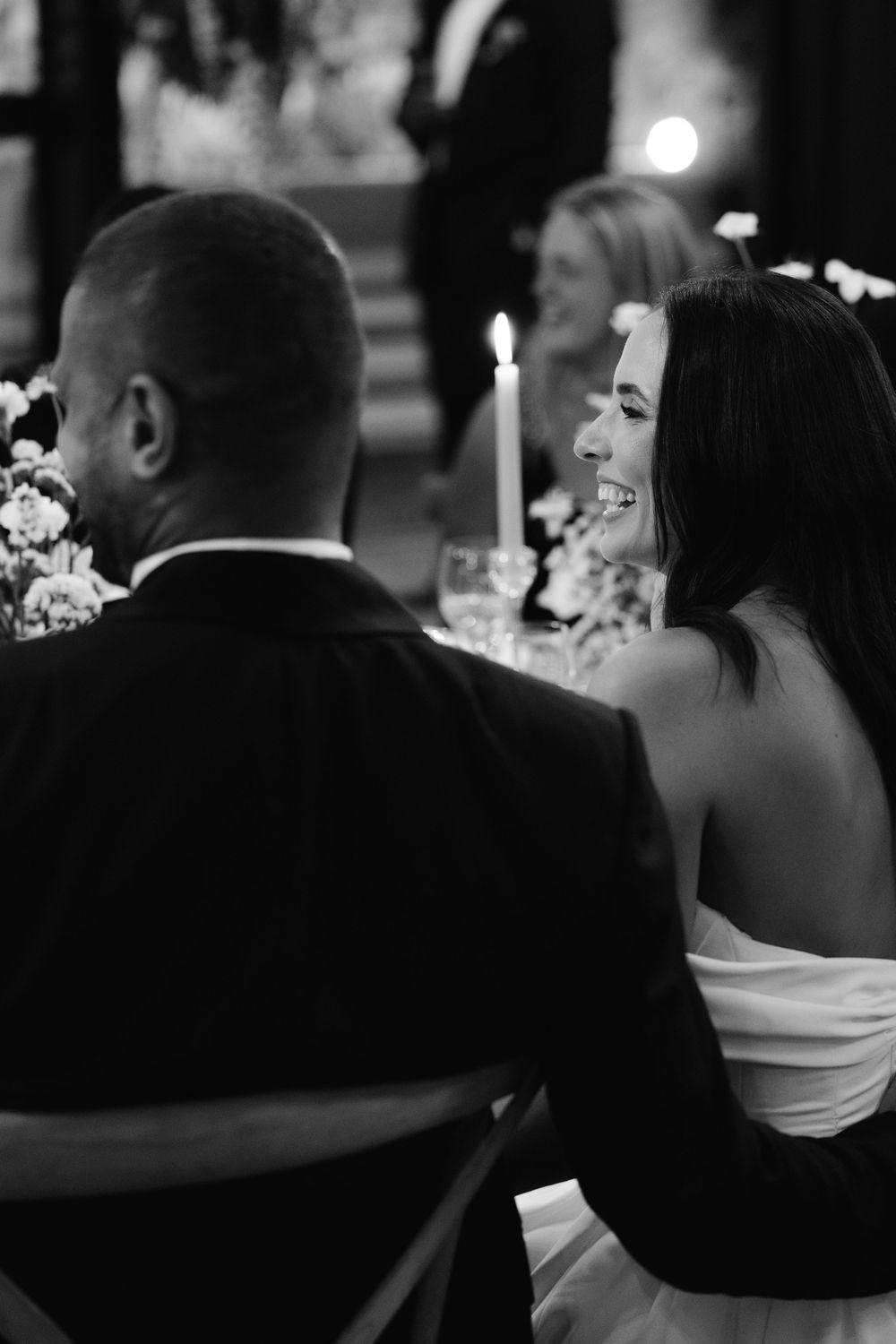 Black and white candid photo of a couple at their wedding reception seated at a table with candlelight.