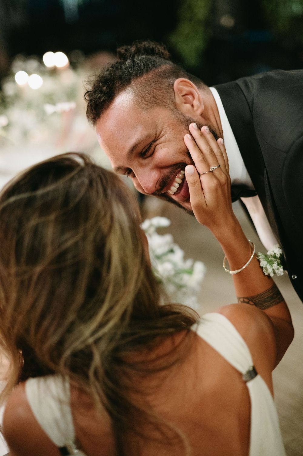 A candid moment between a couple laughing and embracing during what appears to be a wedding celebration.