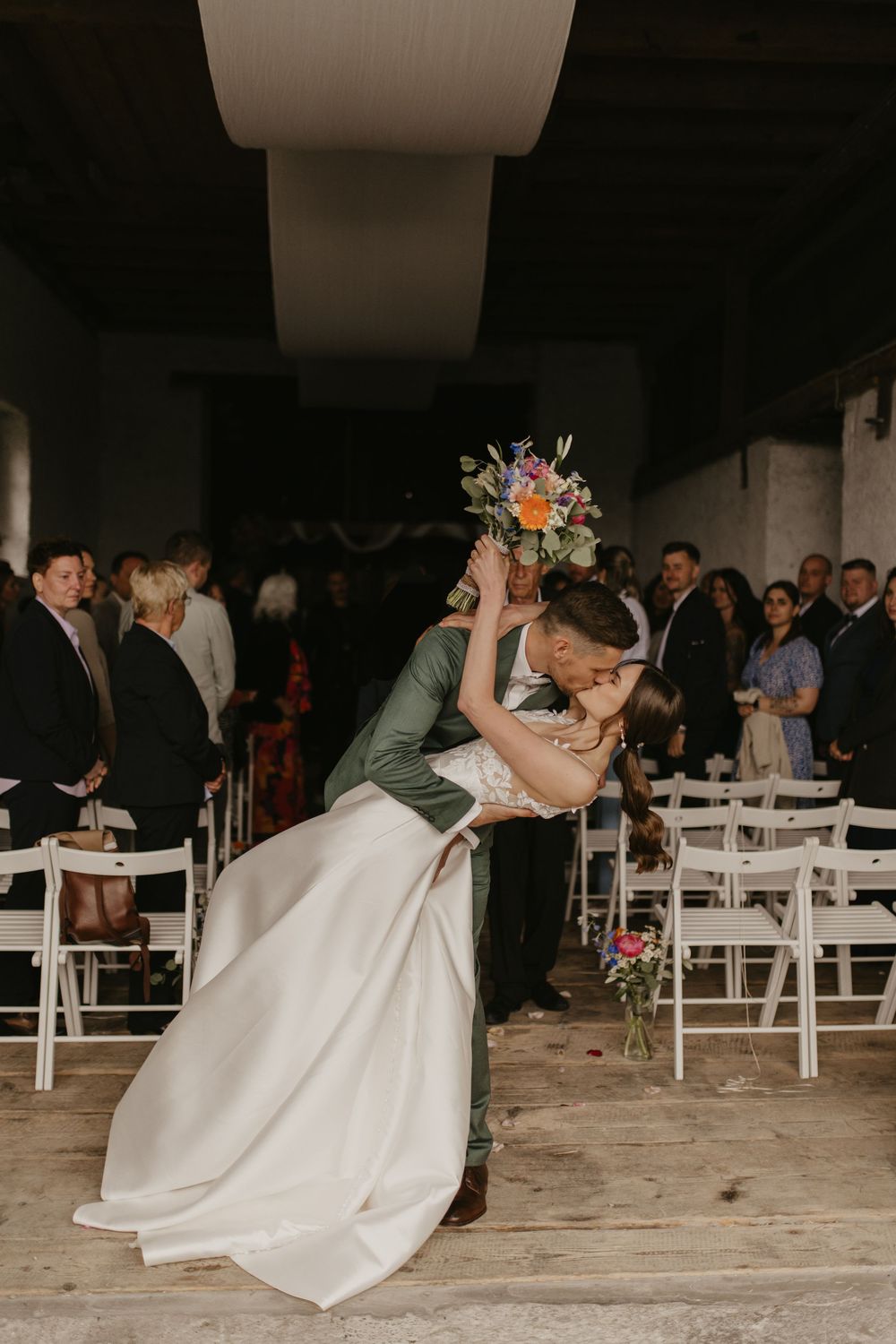 Romantic dance dip during wedding reception with white chairs and floral decorations.