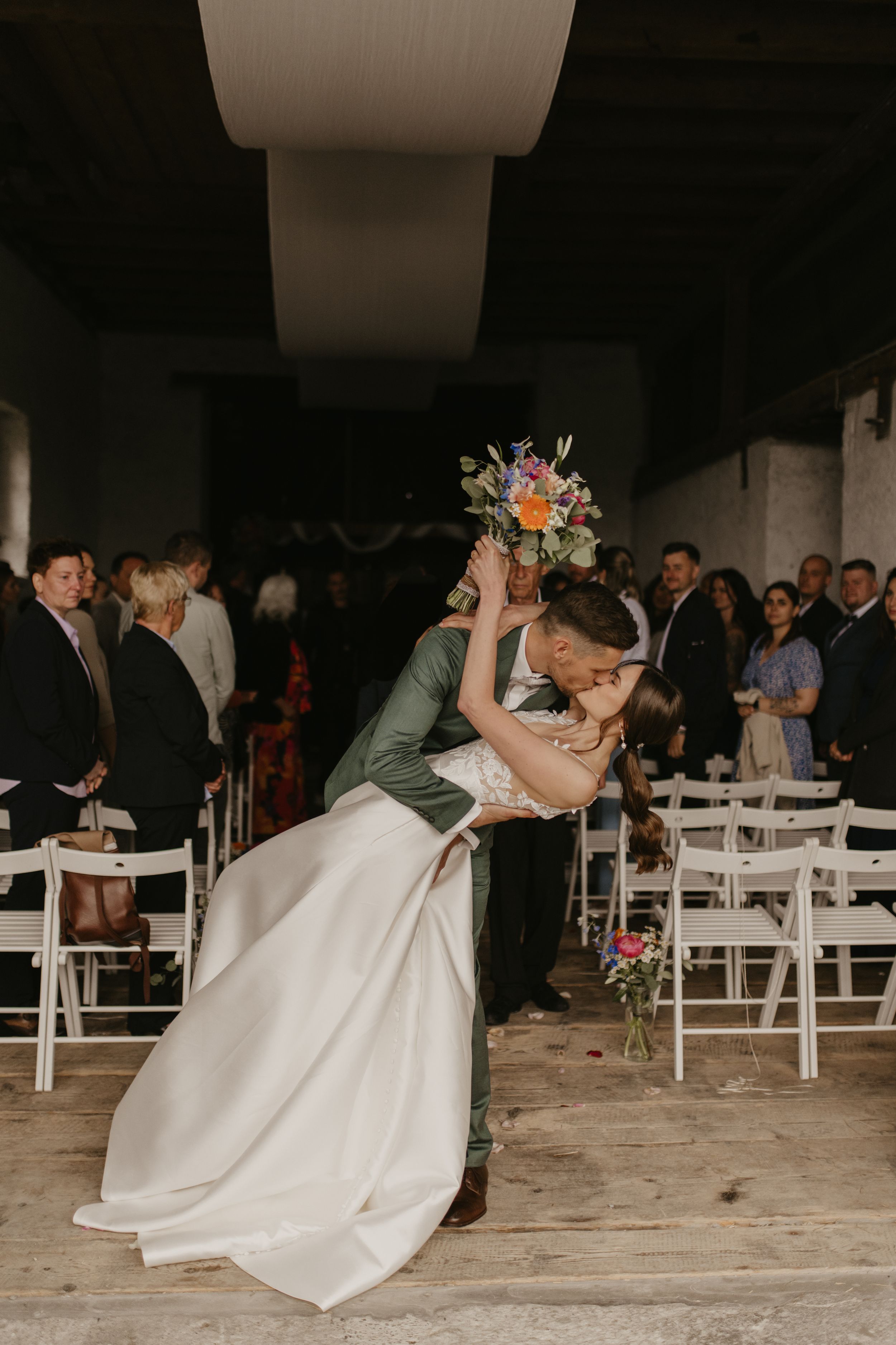 Romantic dance dip during wedding reception with white chairs and floral decorations.