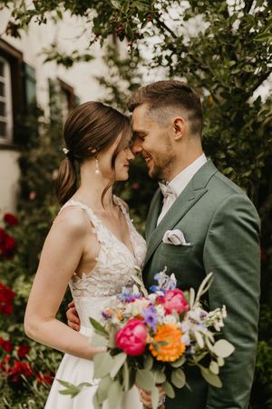 Wedding couple with vibrant floral bouquet sharing intimate moment in garden setting.