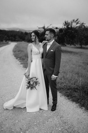 Black and white photo of couple in wedding attire walking along country road.