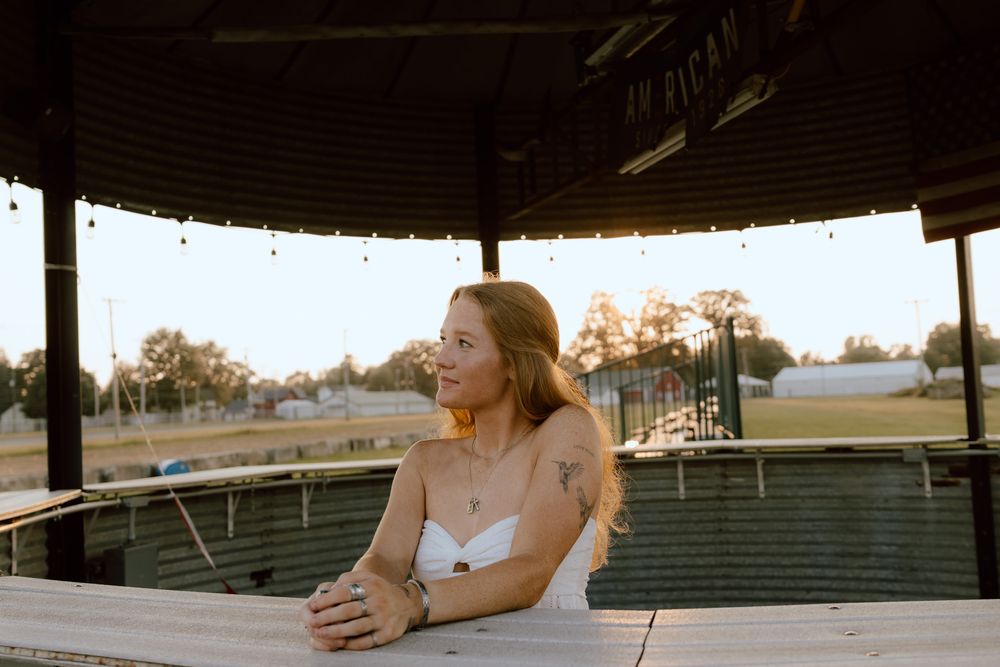 Young woman in white top sitting at wooden table under pavilion at golden hour sunset.