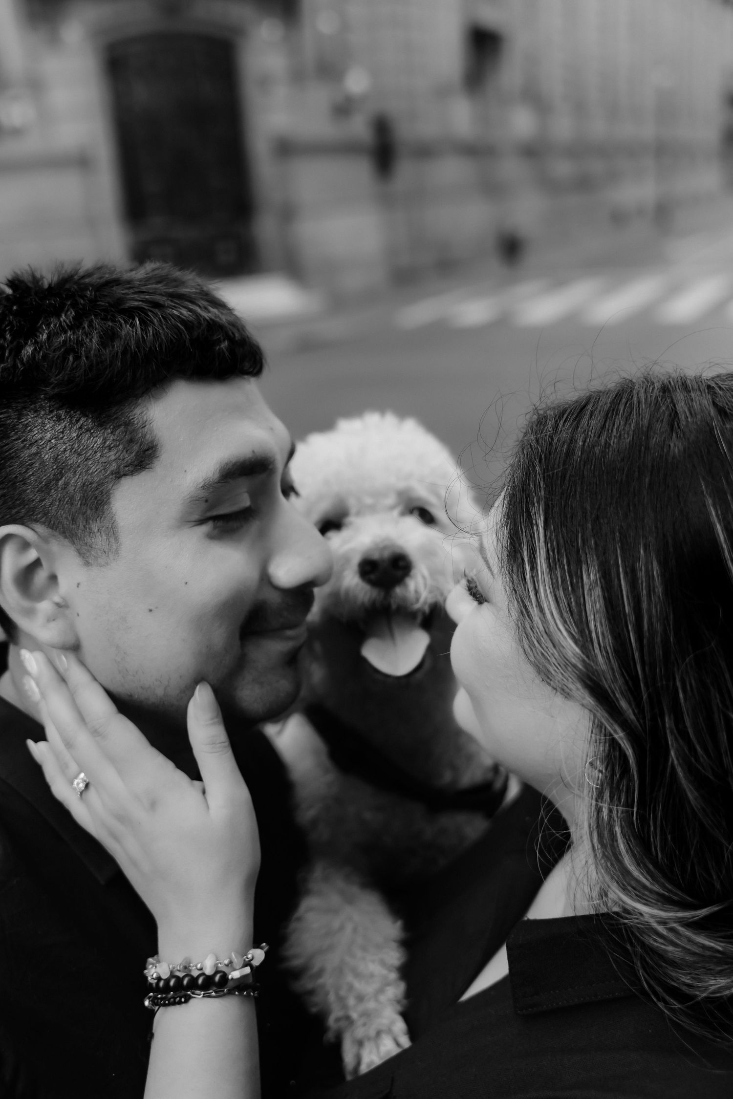 Sweet moment shared between couple and small white dog outdoors in black and white.