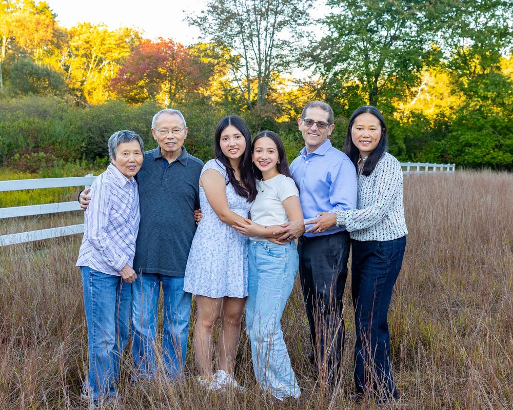 A multi-generational family poses together in a golden field at sunset wearing blue and white outfits for high school senior portraits.