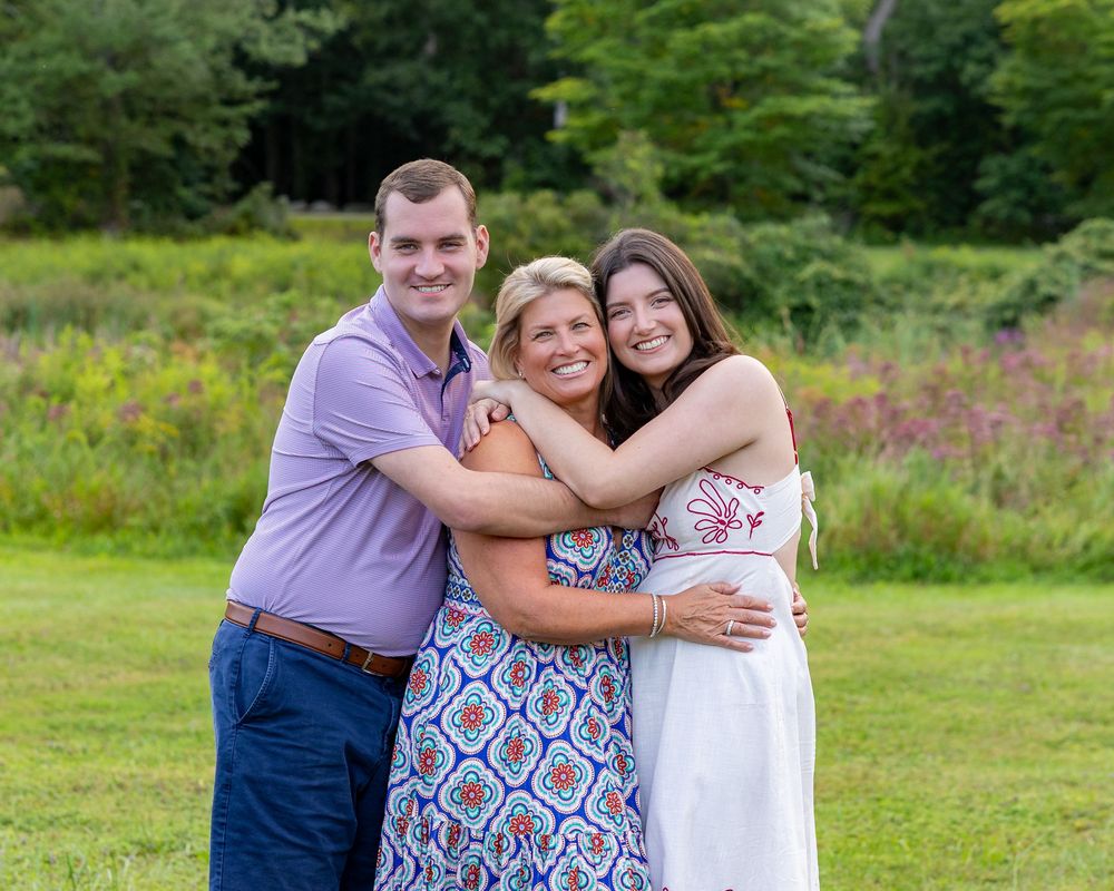 A family poses lovingly together outdoors in a grassy field with wildflowers in the background during a family photoshoot in Lincoln, MA.