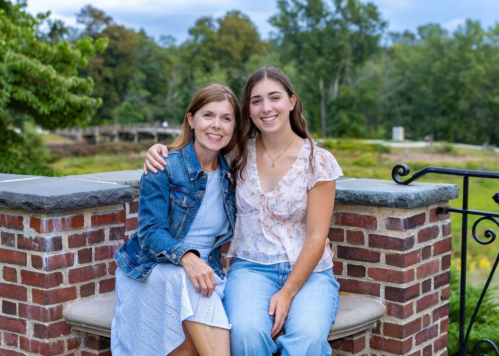 Mother & daughter sit together on a brick wall  surrounded by greenery on a summer day during a high school senior yearbook portraits.