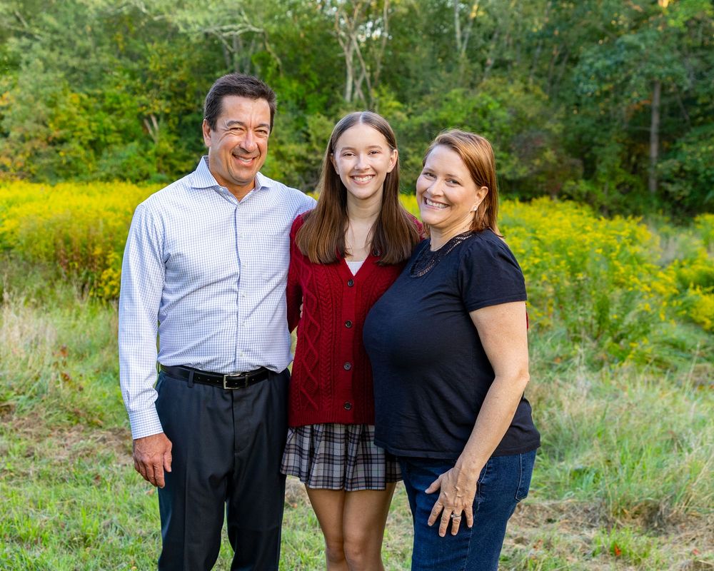 Family shares a warm embrace and laughter while posing together in a lush outdoor setting with yellow wildflowers in Concord, MA.