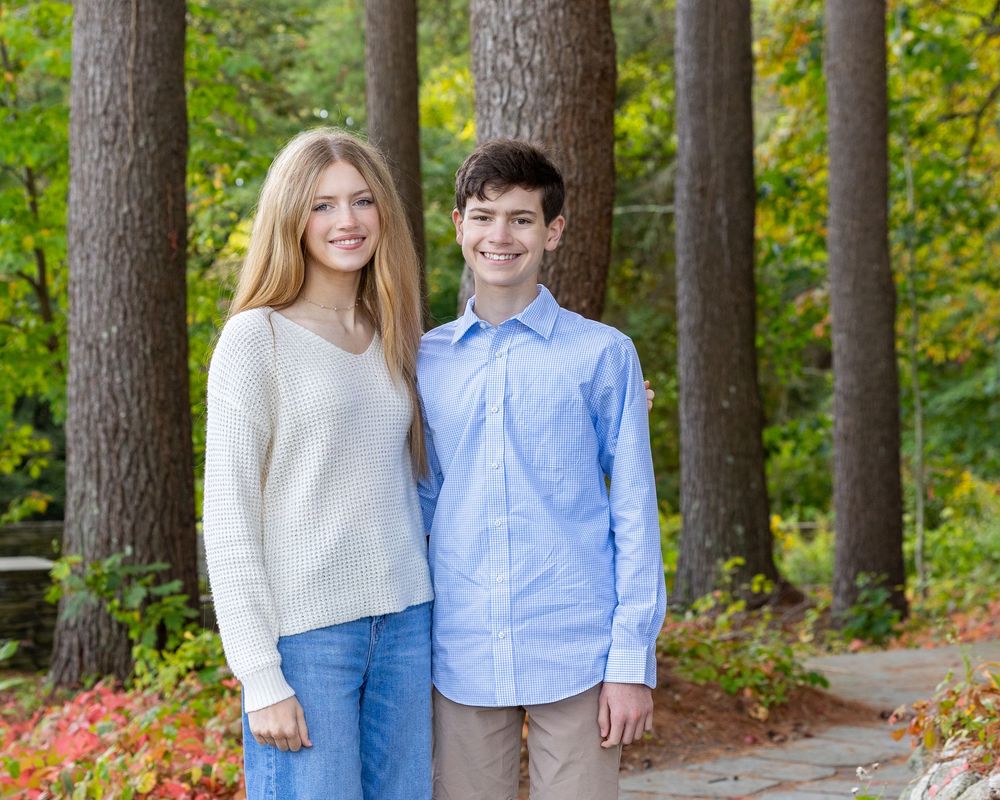 Siblings pose together in coordinated blue & gray outfits against a natural garden backdrop at a fall family photography session in Sudbury.