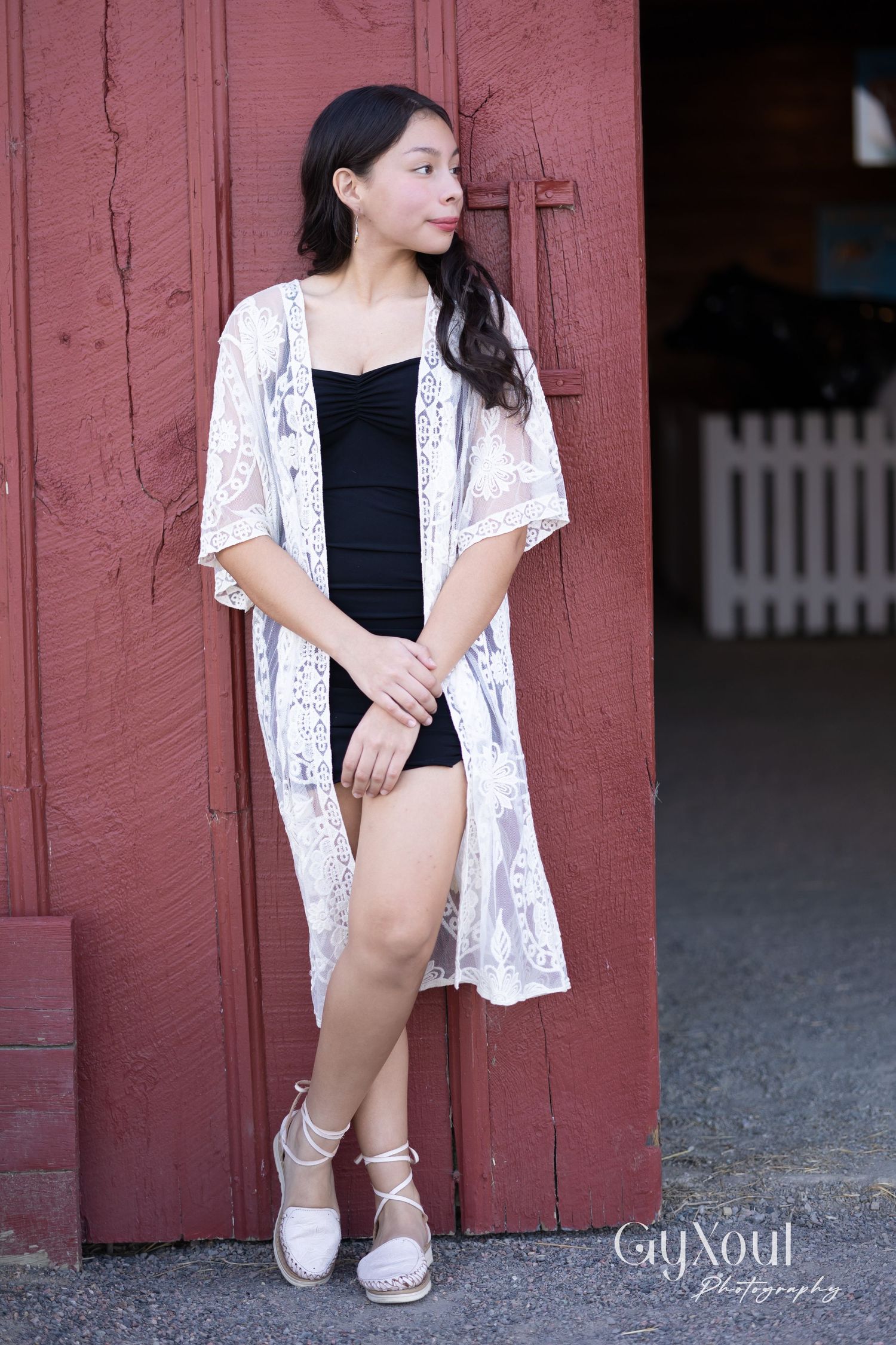 Person wearing lace kimono and black outfit poses against rustic red barn wall.