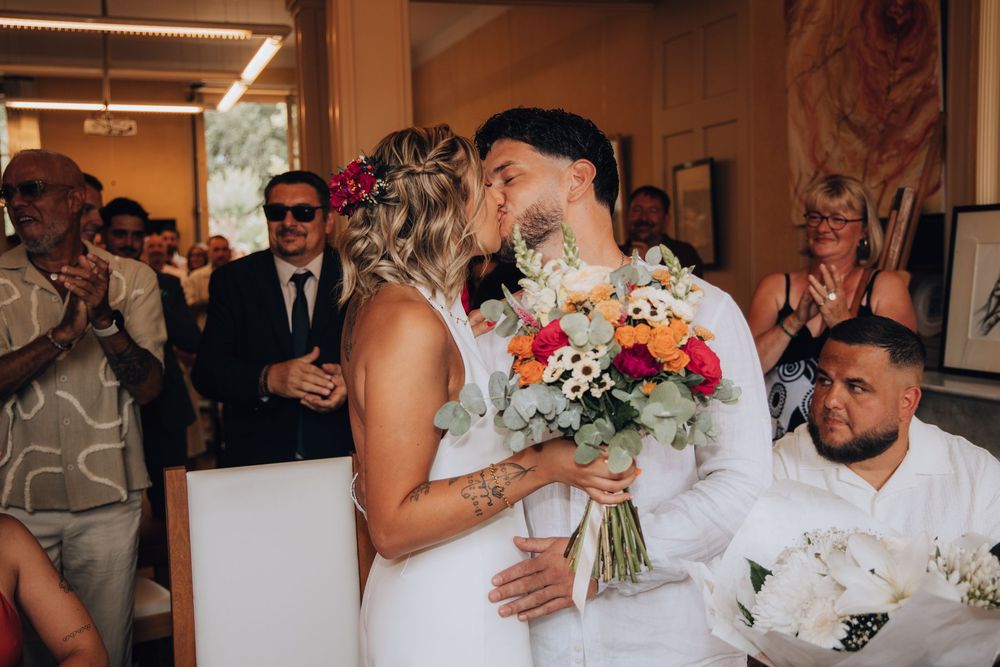 Bride and groom sharing a kiss while guests applaud during their wedding ceremony indoors.