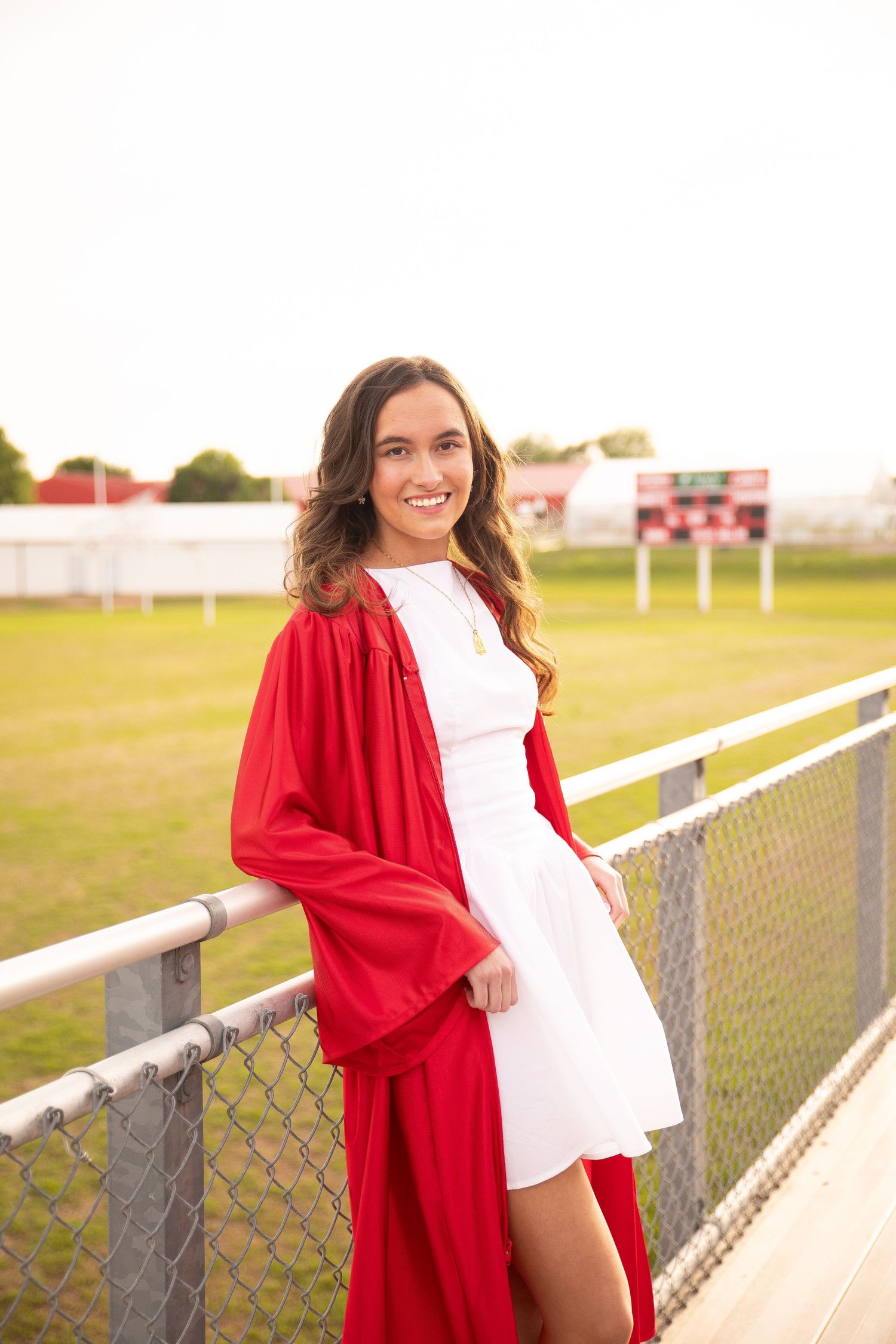A series of graduation photos taken outdoors at a sports field with red gowns and white outfits.