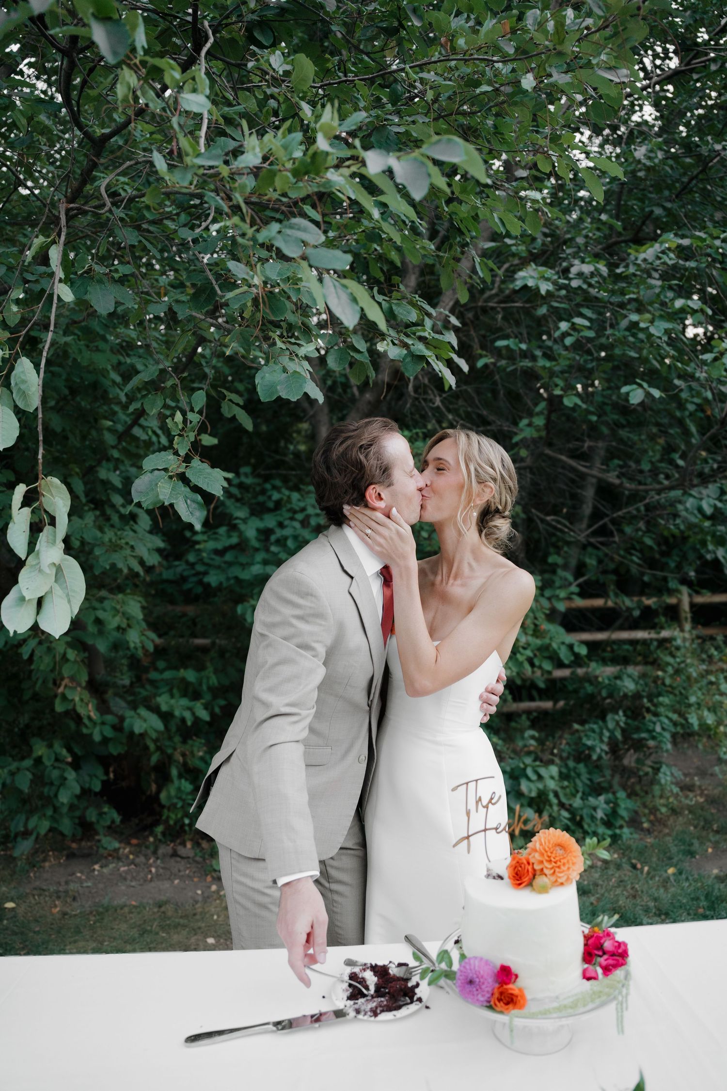 A romantic moment shared between newlyweds at their wedding cake cutting ceremony in an outdoor garden setting.
