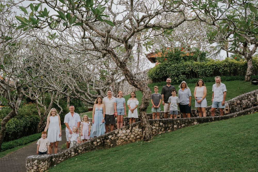 A group of people stand together in coordinated white and gray outfits under blooming cherry blossom trees.
