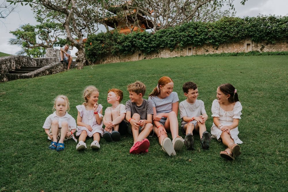 Group of people sitting together in a row on lush green grass during a sunny outdoor gathering.