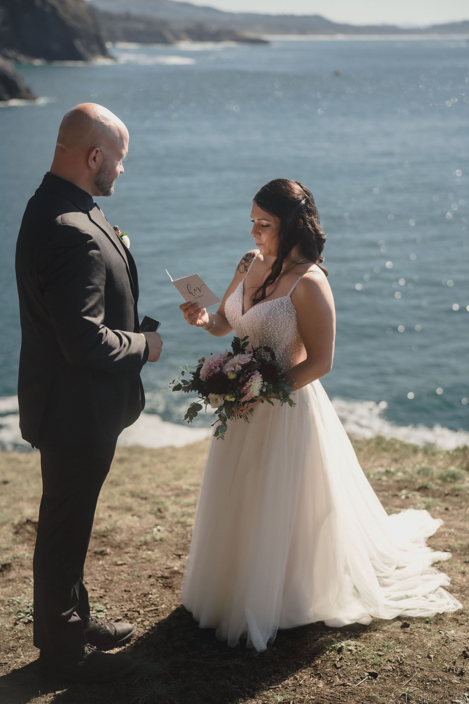 A couple in wedding attire exchanges vows on a scenic coastal cliff overlooking the ocean during their intimate ceremony.