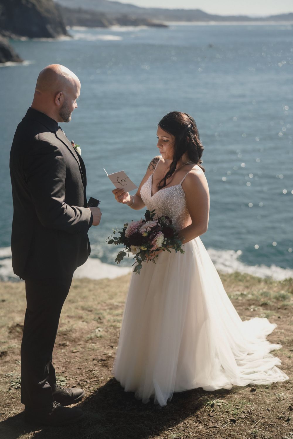 A couple in wedding attire exchanges vows on a scenic coastal cliff overlooking the ocean during their intimate ceremony.
