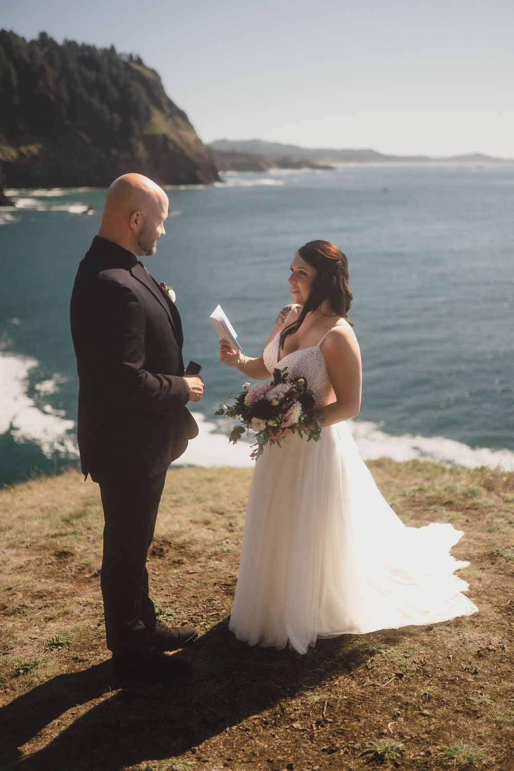 A wedding couple exchanges vows on a scenic coastal cliff overlooking the Pacific Ocean during their intimate ceremony.