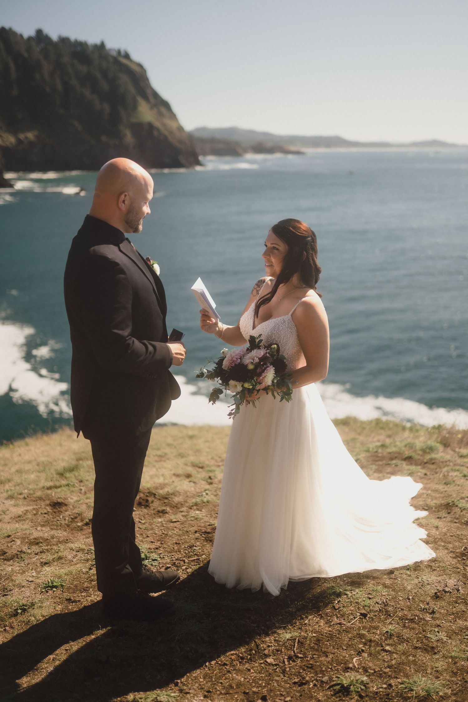 A wedding couple exchanges vows on a scenic coastal cliff overlooking the Pacific Ocean during their intimate ceremony.