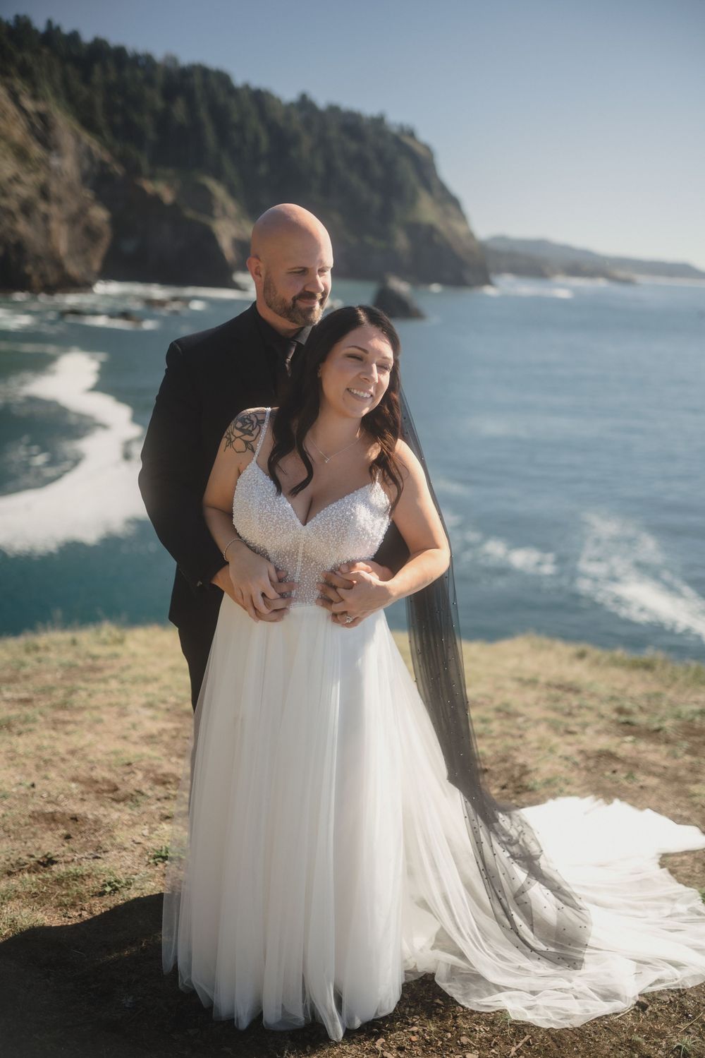 A couple shares a joyful moment together on a scenic coastal cliff overlooking the ocean on their wedding day.