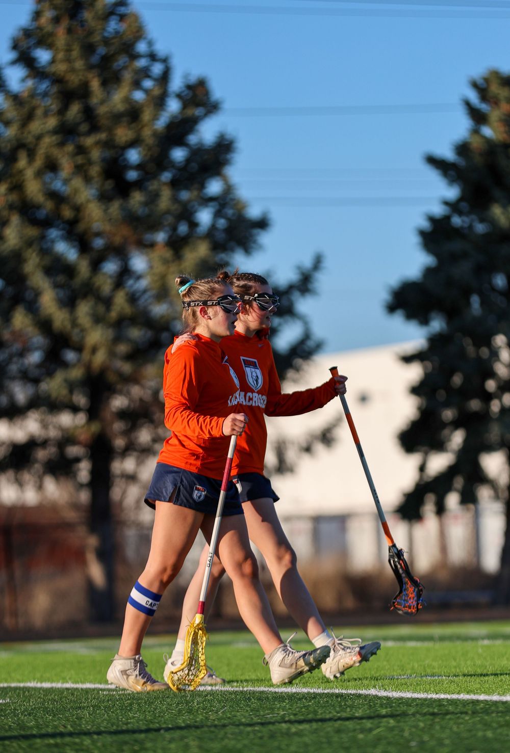Athletes in orange uniforms practice lacrosse drills on a grass field.