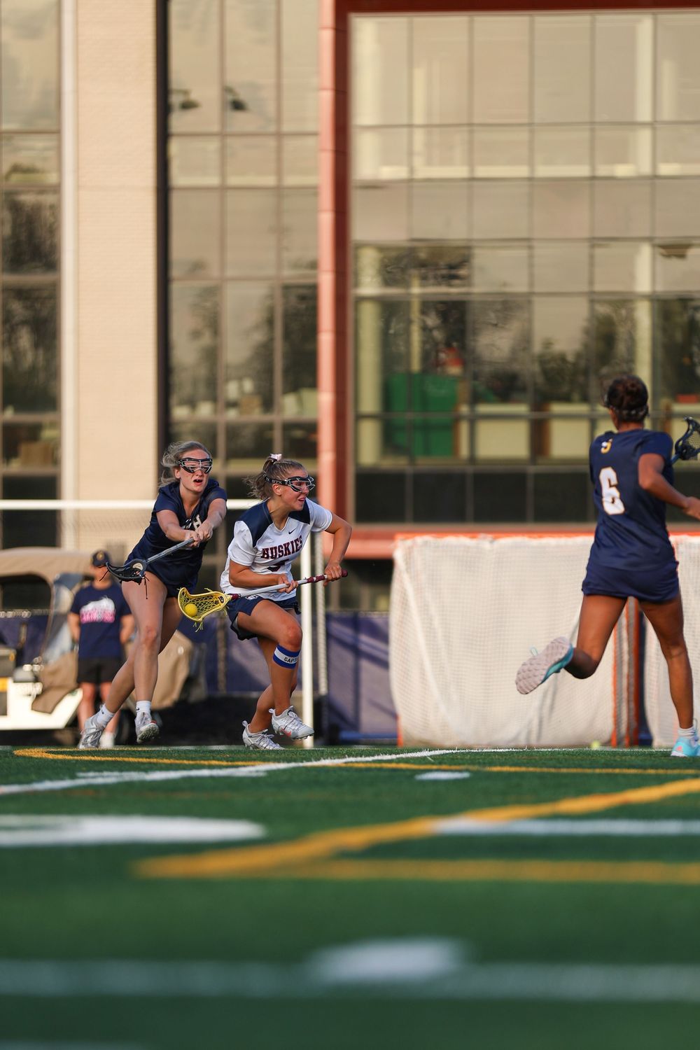 Team stretching in formation on artificial turf field near campus buildings.