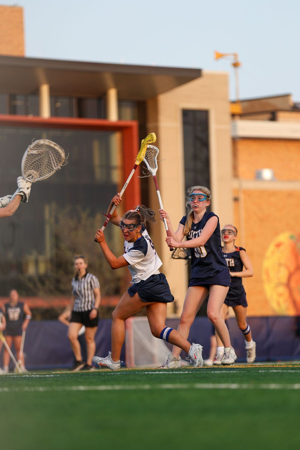 Lacrosse players practicing drills during golden hour on athletic field.