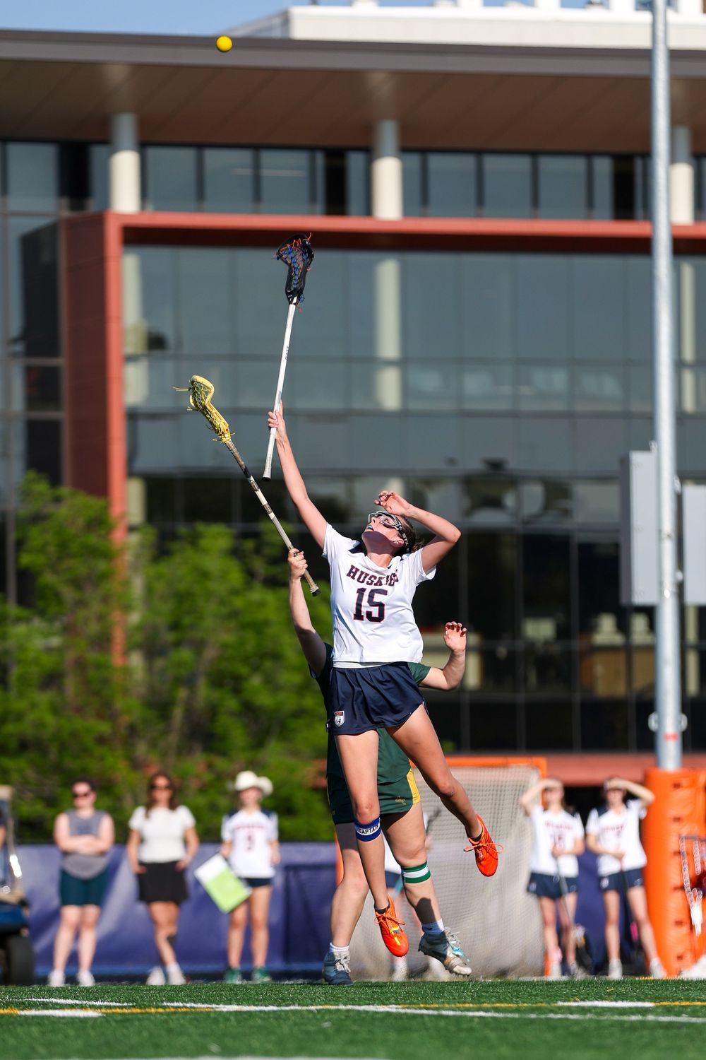 Lacrosse players practicing on field with a yellow ball in midair.