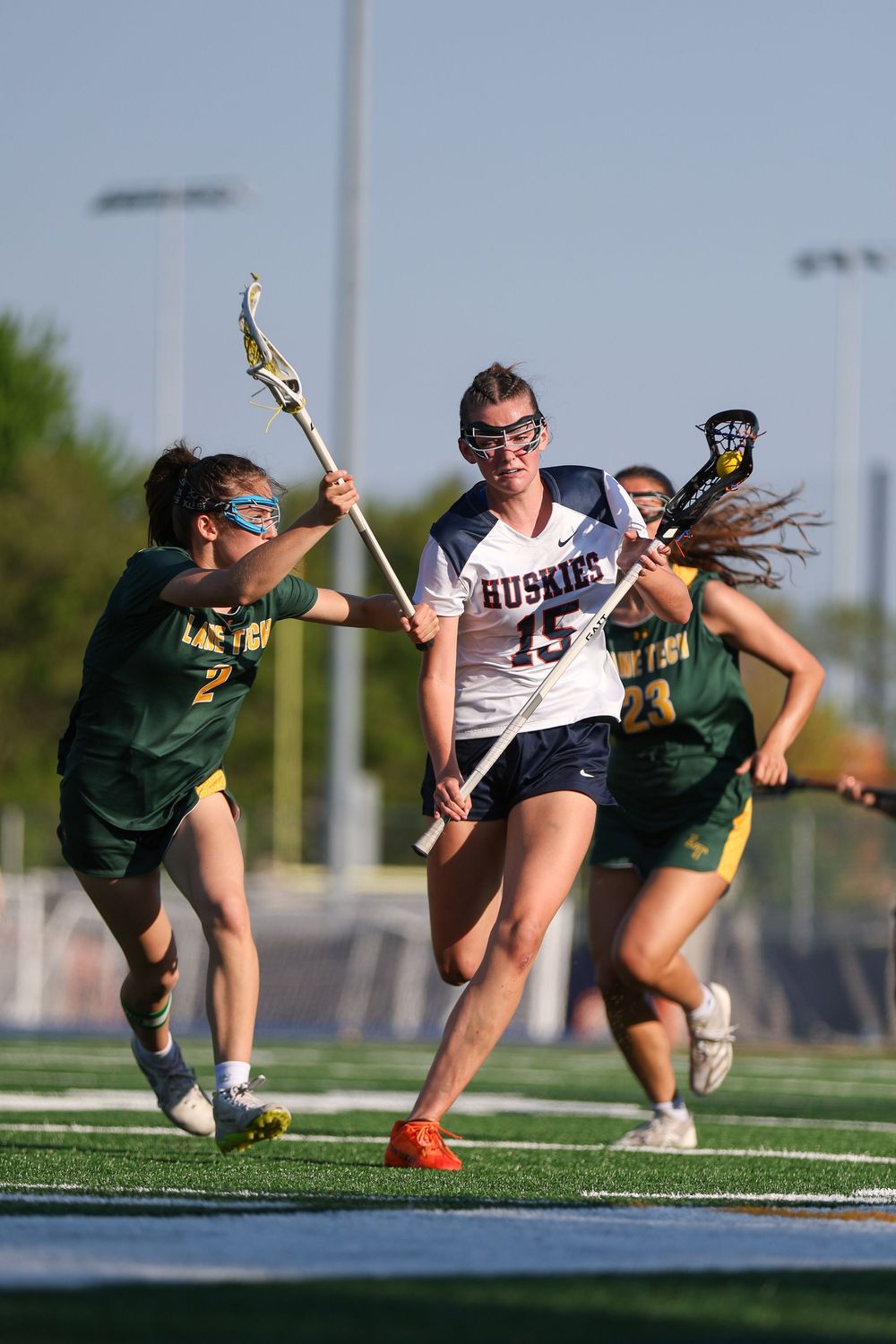Lacrosse players competing intensely during a match between teams in white and green uniforms.