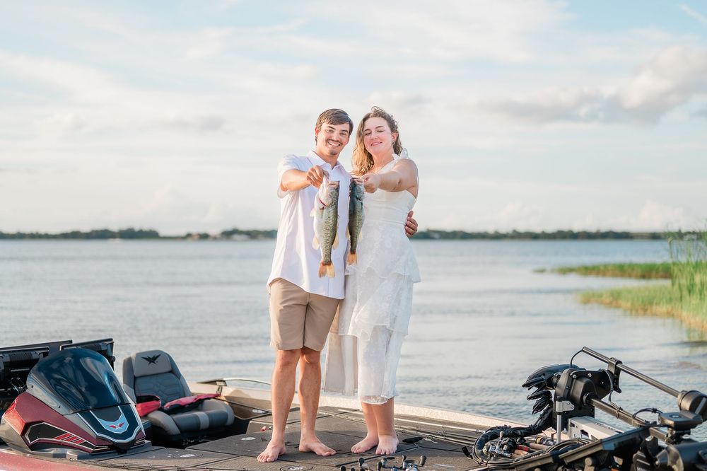 A couple stands on a wooden dock by a lake with bicycles and bags nearby on a sunny summer day.