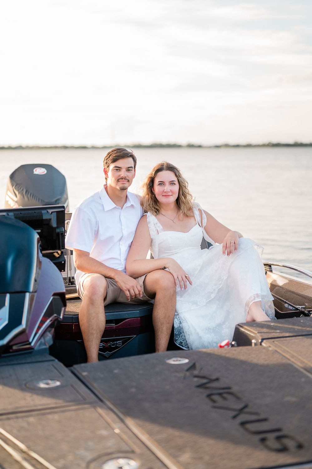 Couple sitting together on a wooden dock during sunset wearing white and casual attire.