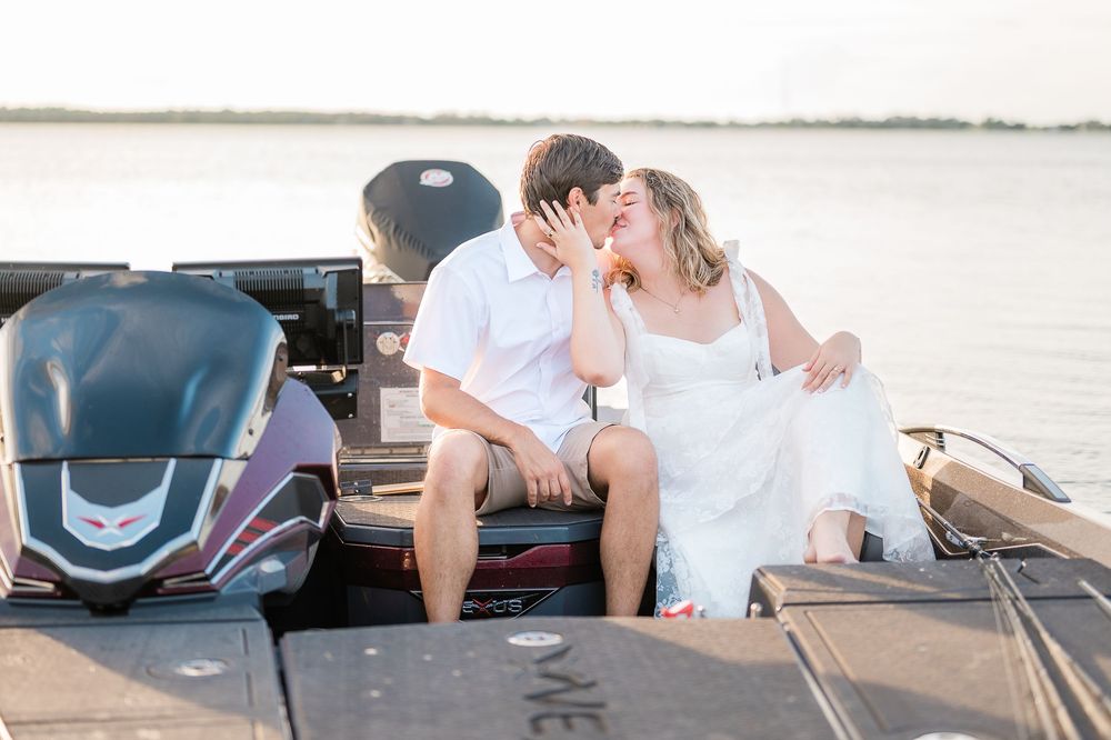 A romantic couple shares an intimate moment while sitting on a boat dock at sunset near the water.
