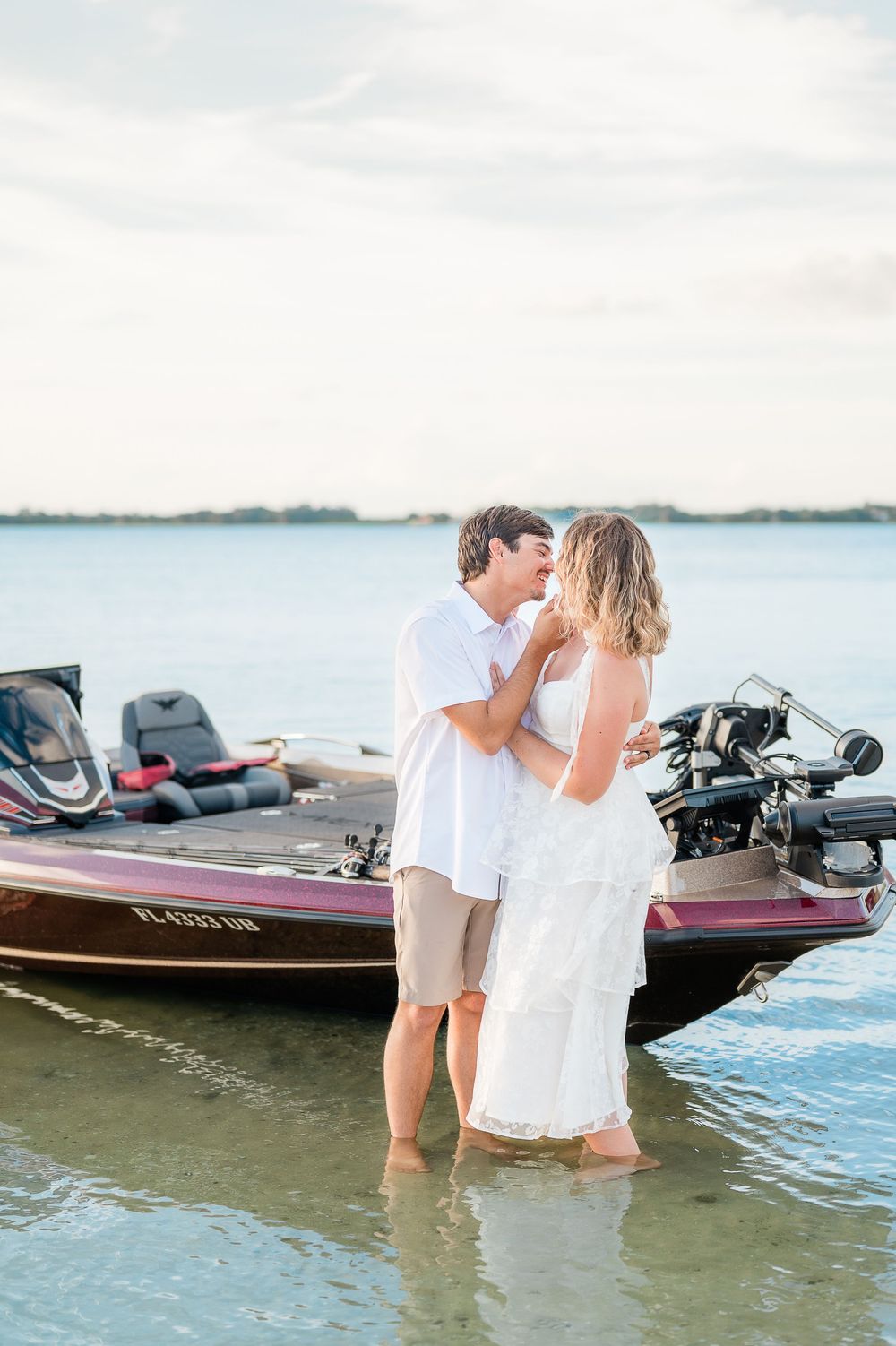 A romantic couple shares an intimate moment while standing in shallow water next to a fishing boat at sunset.