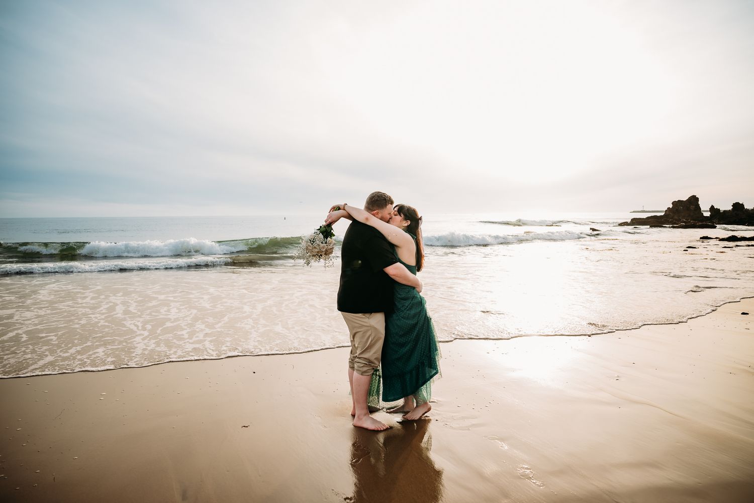A couple hugs while standing in the ocean waves at sunset.
