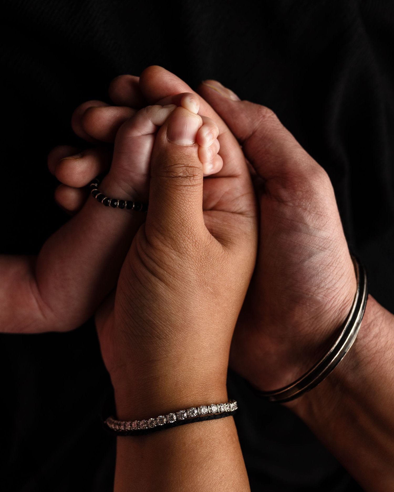 Two hands wearing silver bracelets clasp together intimately against a dark background.