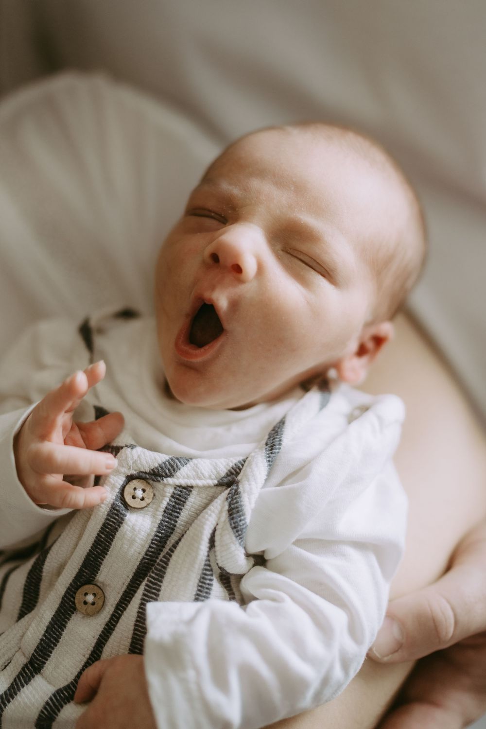 Baby wearing striped outfit reaching up playfully while lying down.
