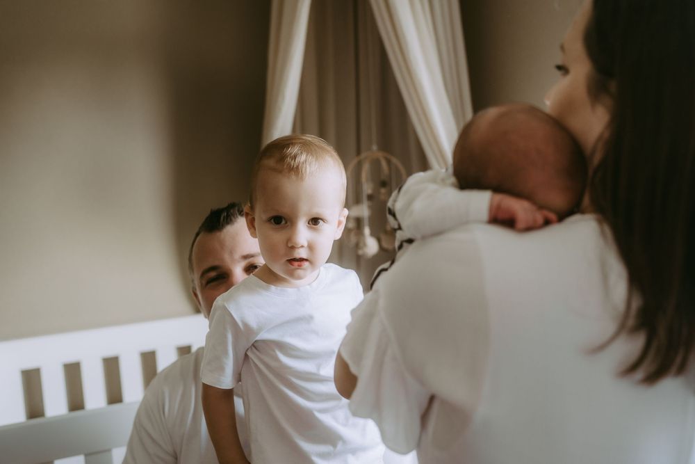 Family bonding moment in nursery with white crib and curtains.