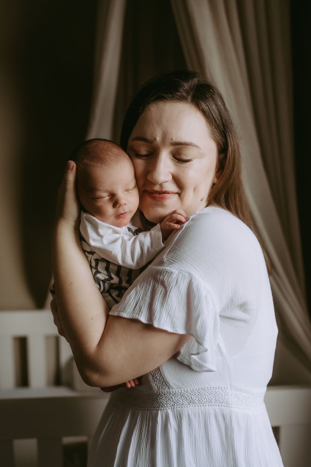 A tender moment of embrace between parent and baby in white clothing against a dark background.