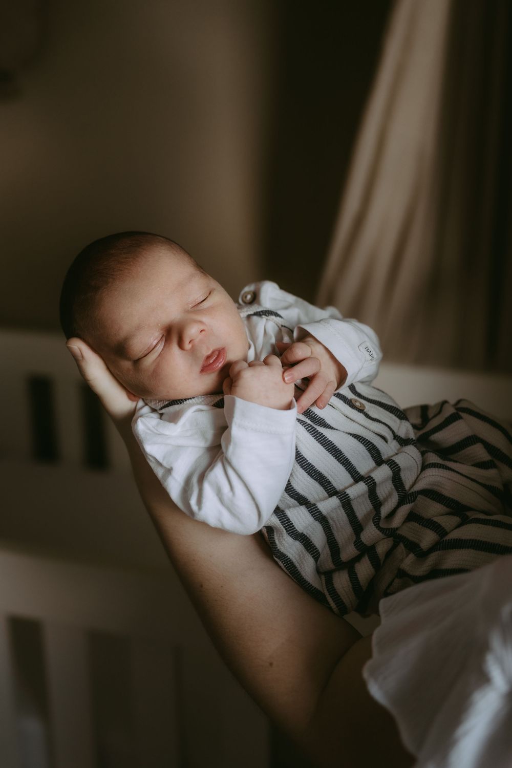 Sleeping baby in striped outfit rests peacefully in a moody indoor setting.