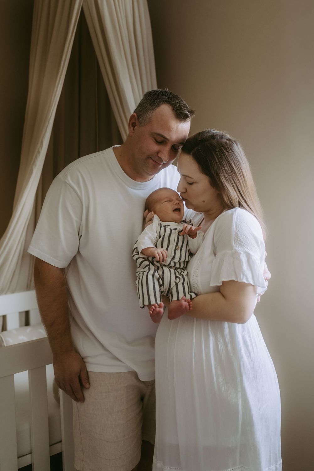 Couple in white clothing share an intimate moment together against neutral backdrop.
