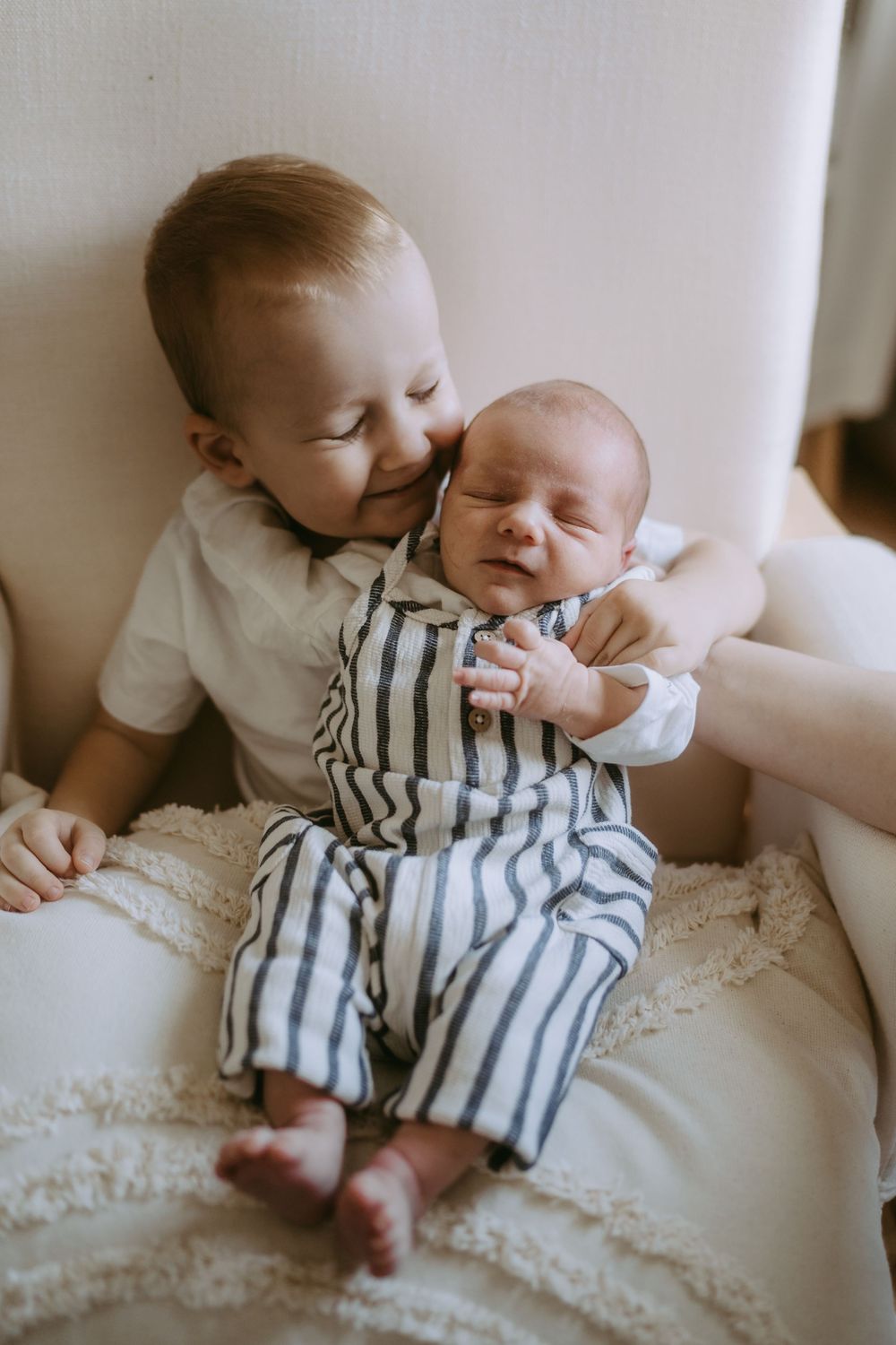 Baby in striped outfit rests on white textured surface in natural light.