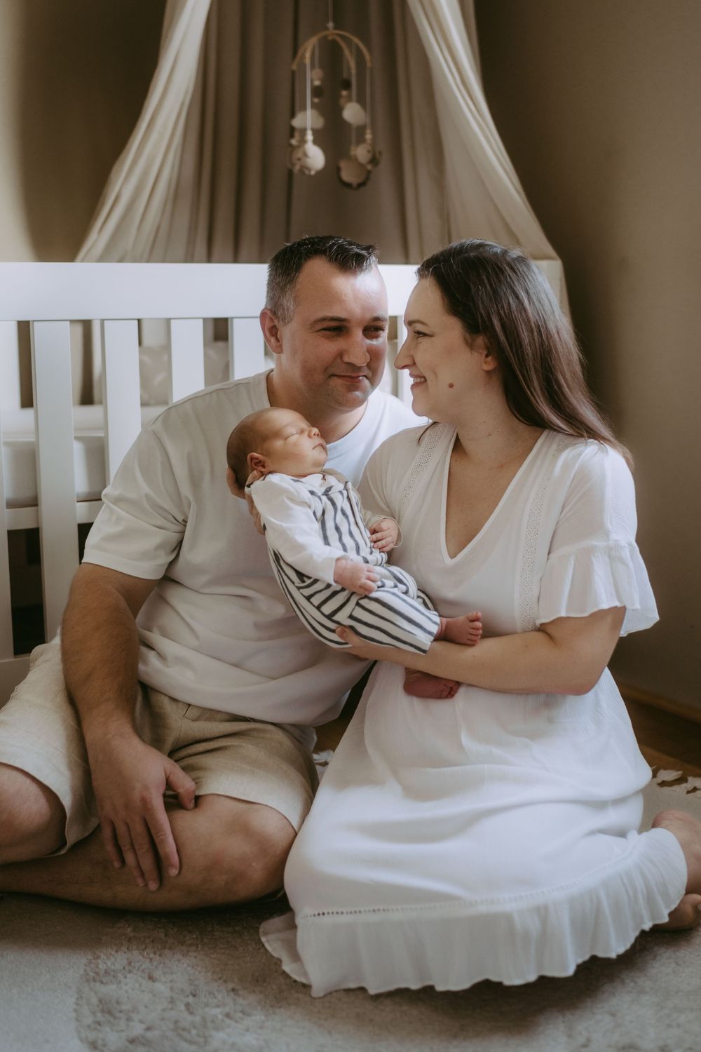 Family shares tender moments together on white bedding in muted tones.
