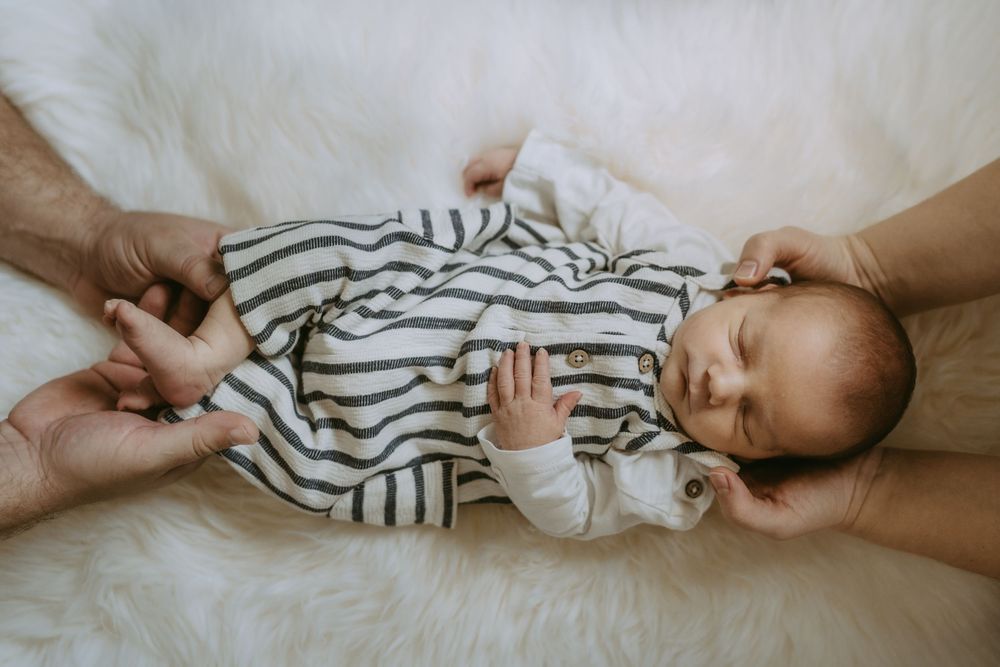 Baby in striped outfit lies peacefully on white surface with hands visible.