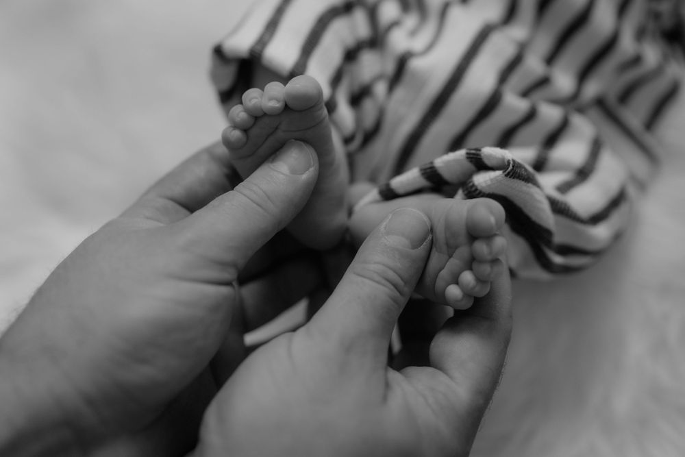 Close-up detail of hands tenderly touching baby in striped clothing.