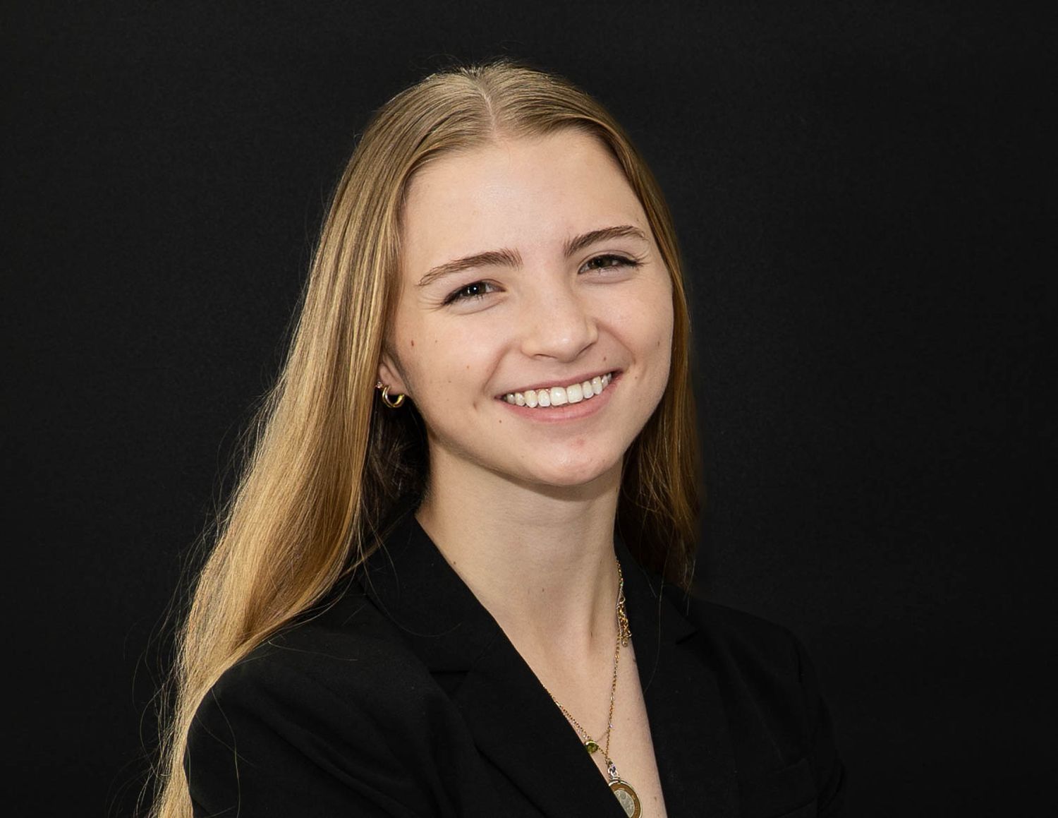 Professional headshot of someone with long blonde hair wearing a black top against a dark background.