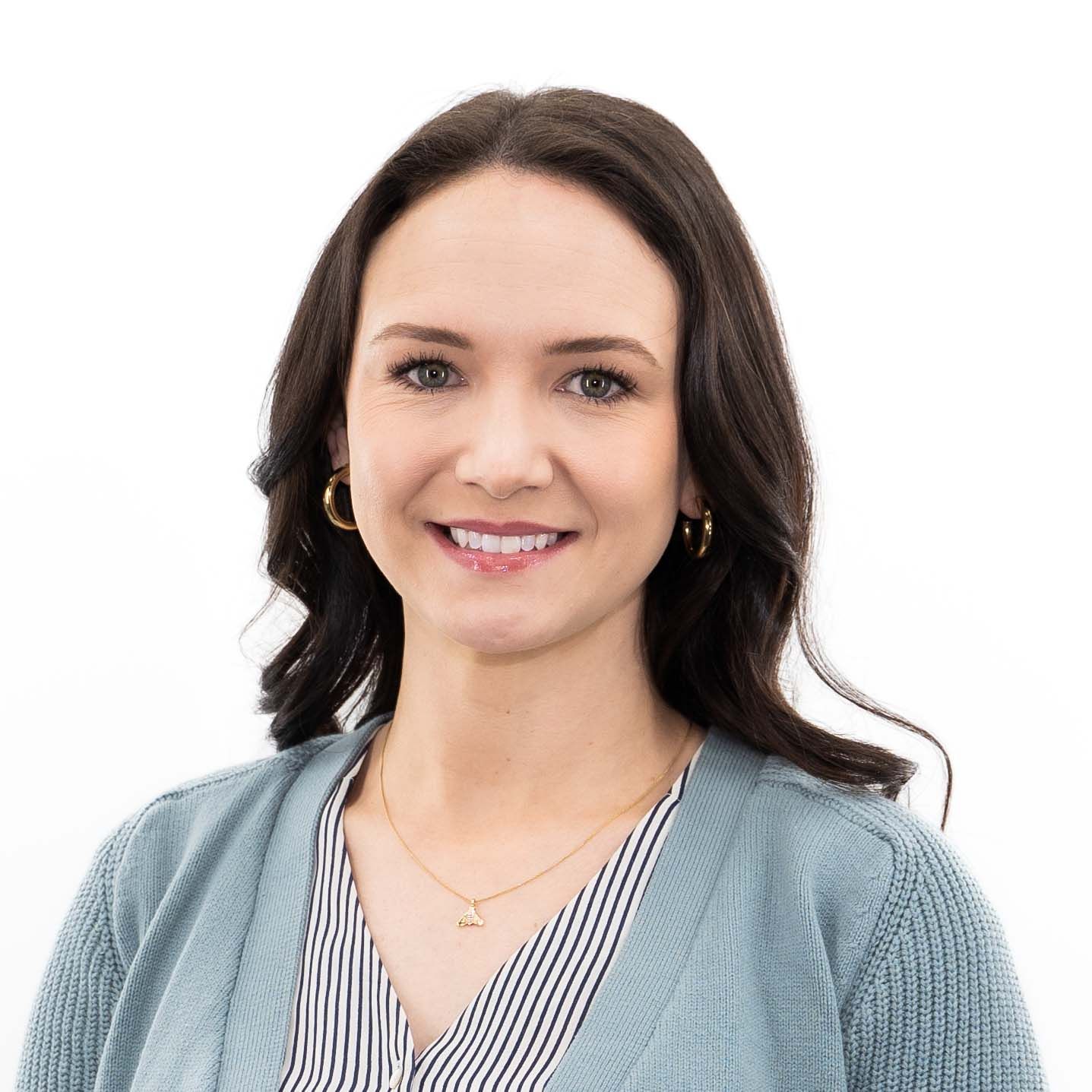 Professional headshot of someone with dark hair wearing a gray cardigan and striped blouse against white background.