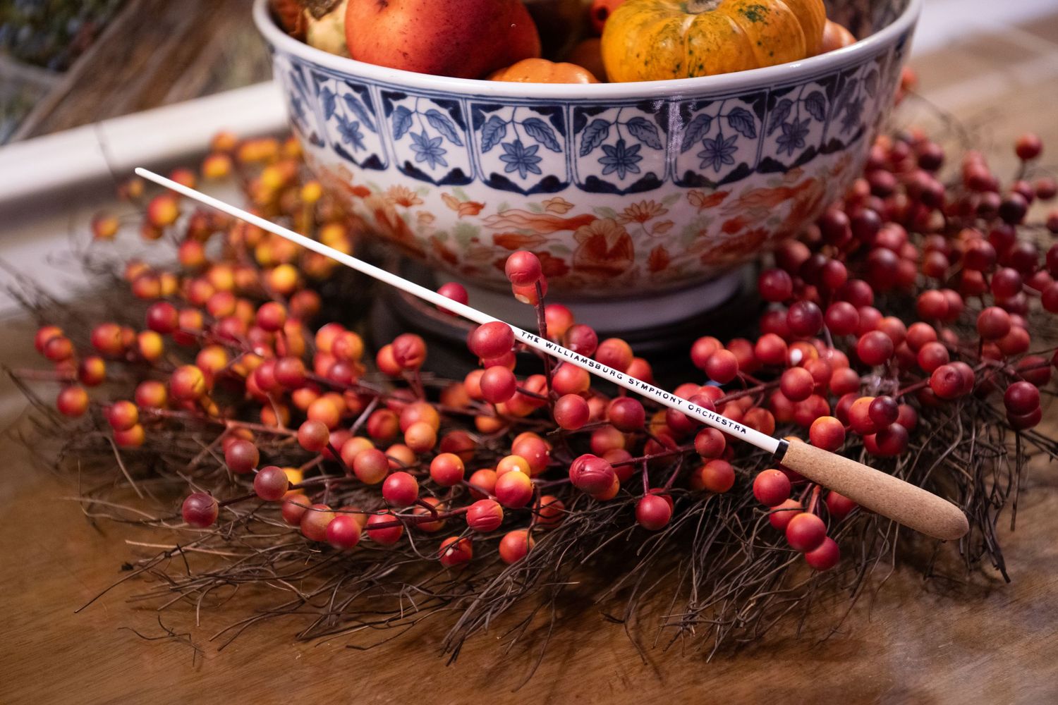 Red berries and pine needles wreath surrounding a decorative bowl filled with autumn fruits on a wooden table. Best photographer Williamsbur